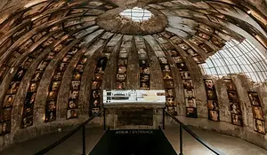 Interior of Bunk’Art 2 in Tirana, Albania, showing a circular concrete bunker lined with portrait photographs and a central entrance below a skylight.