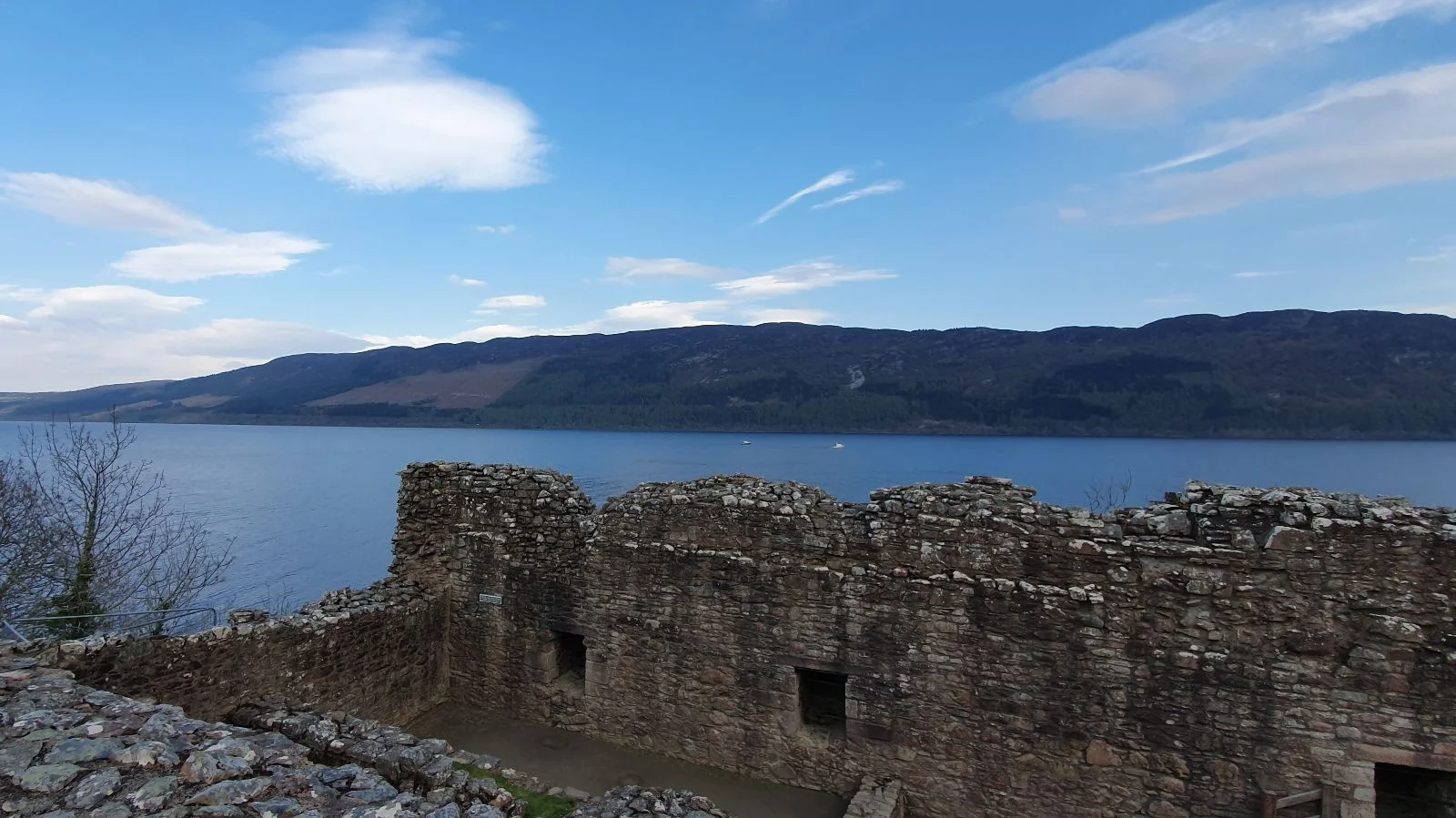 View from Urquhart Castle ruins overlooking Loch Ness, with stone walls in the foreground and hills across the water.