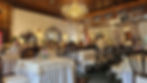 Elegant restaurant with chandeliers and ornate mirrors. People dine around tables, musicians play instruments. Sign reads "Silver Room."