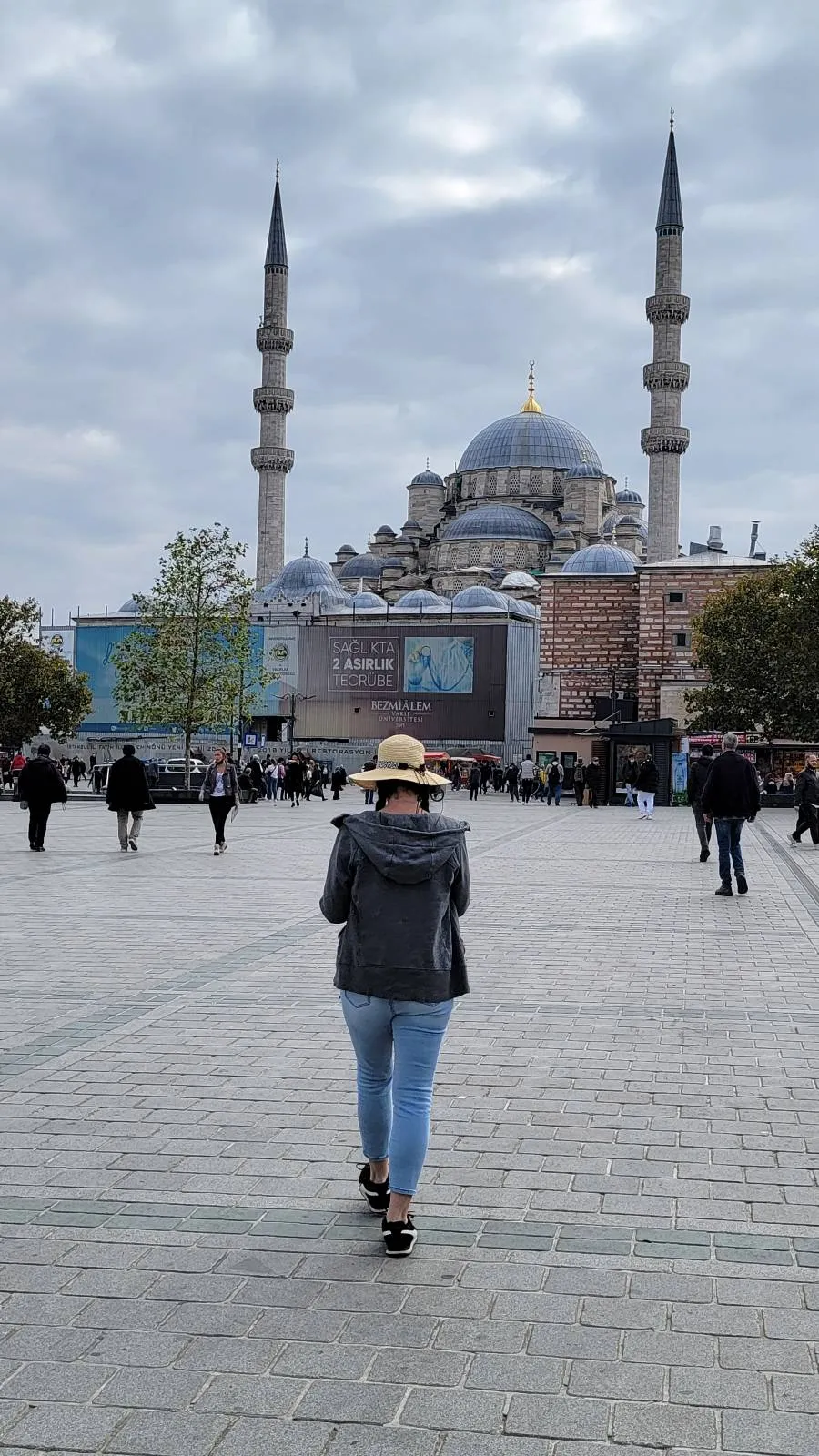 Person walking toward a large mosque with two minarets under a cloudy sky.