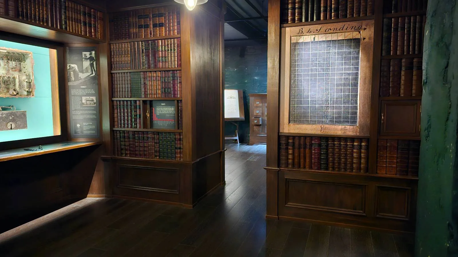 Dimly lit library room with wooden bookcases filled with books and a glass partition reflecting the light.