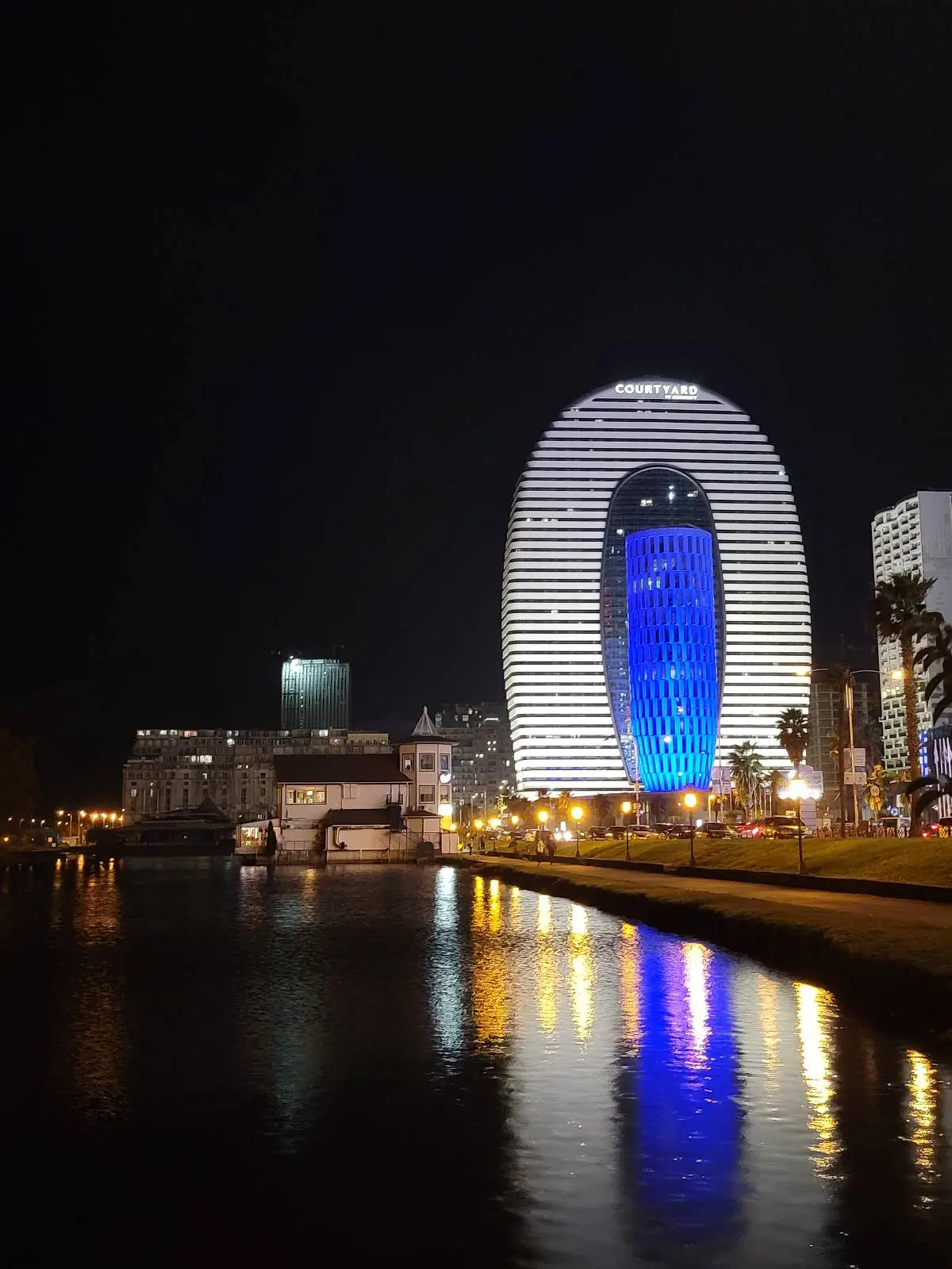 White oval shaped Marriot Hotel Building at night, with reflection glistening in the black sea water coast.