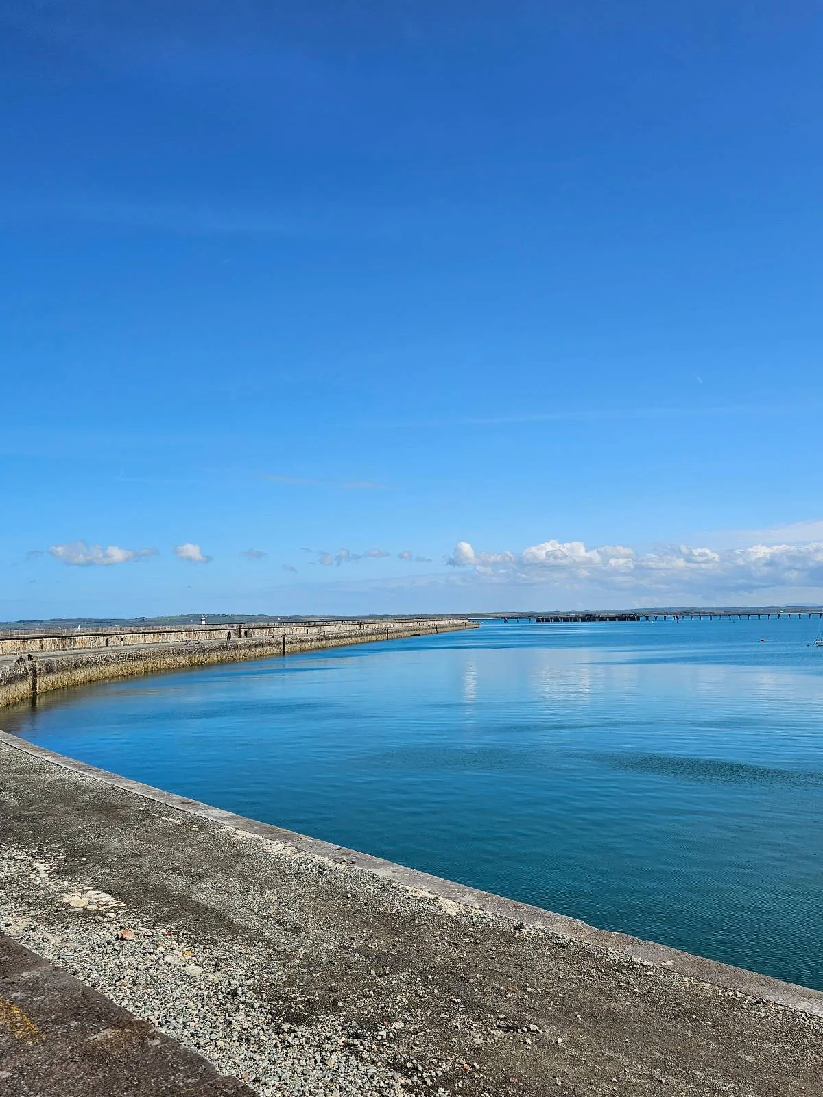 A calm, expansive seawater pool bordered by a stone breakwater under a clear blue sky.