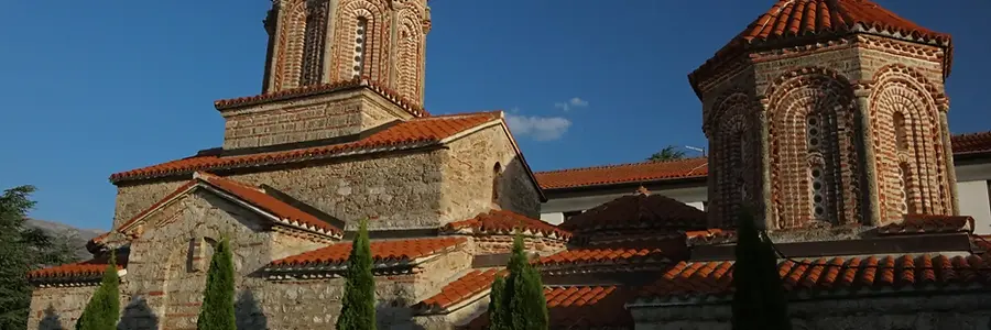 The historic stone buildings and brick dome of the St. Naum Monastery under a bright blue sky on the North Macedonia travel guide.