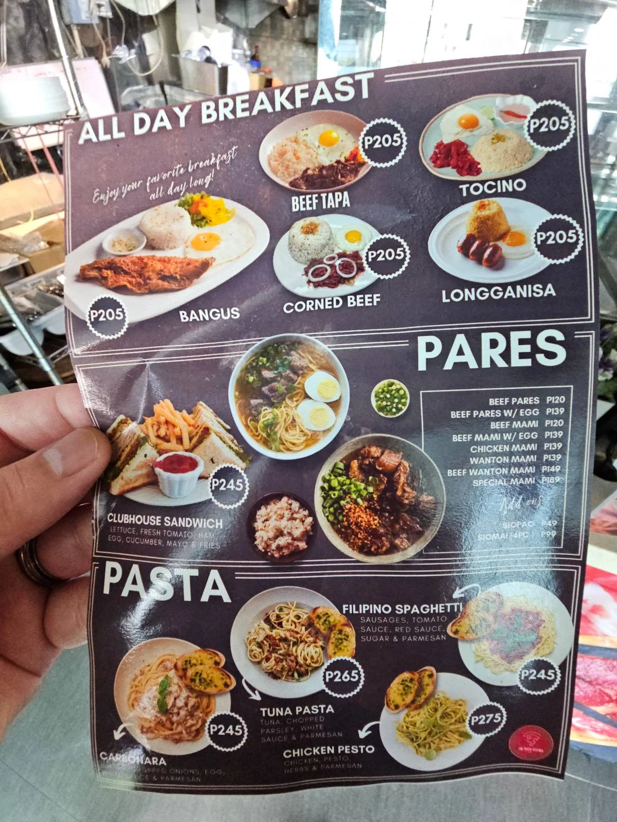 A hand holds a menu with food images and prices. The top section features breakfast items like red tapa, tocino, and longganisa. The middle section lists pares dishes. The bottom section offers pasta options such as tuna pasta and Filipino spaghetti.