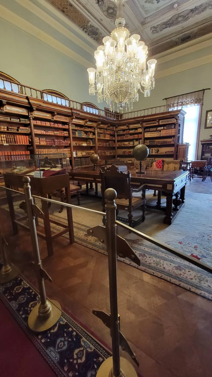 Room with wooden bookshelves filled with books, a large chandelier, and a wooden table and chairs. A rope barrier separates the area.
