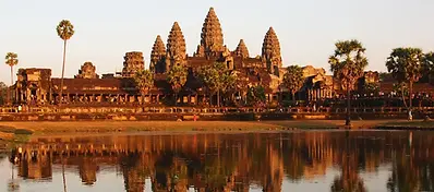 The iconic Angkor Wat temple complex at sunset, with its five central towers reflected perfectly in the still water of the surrounding moat.