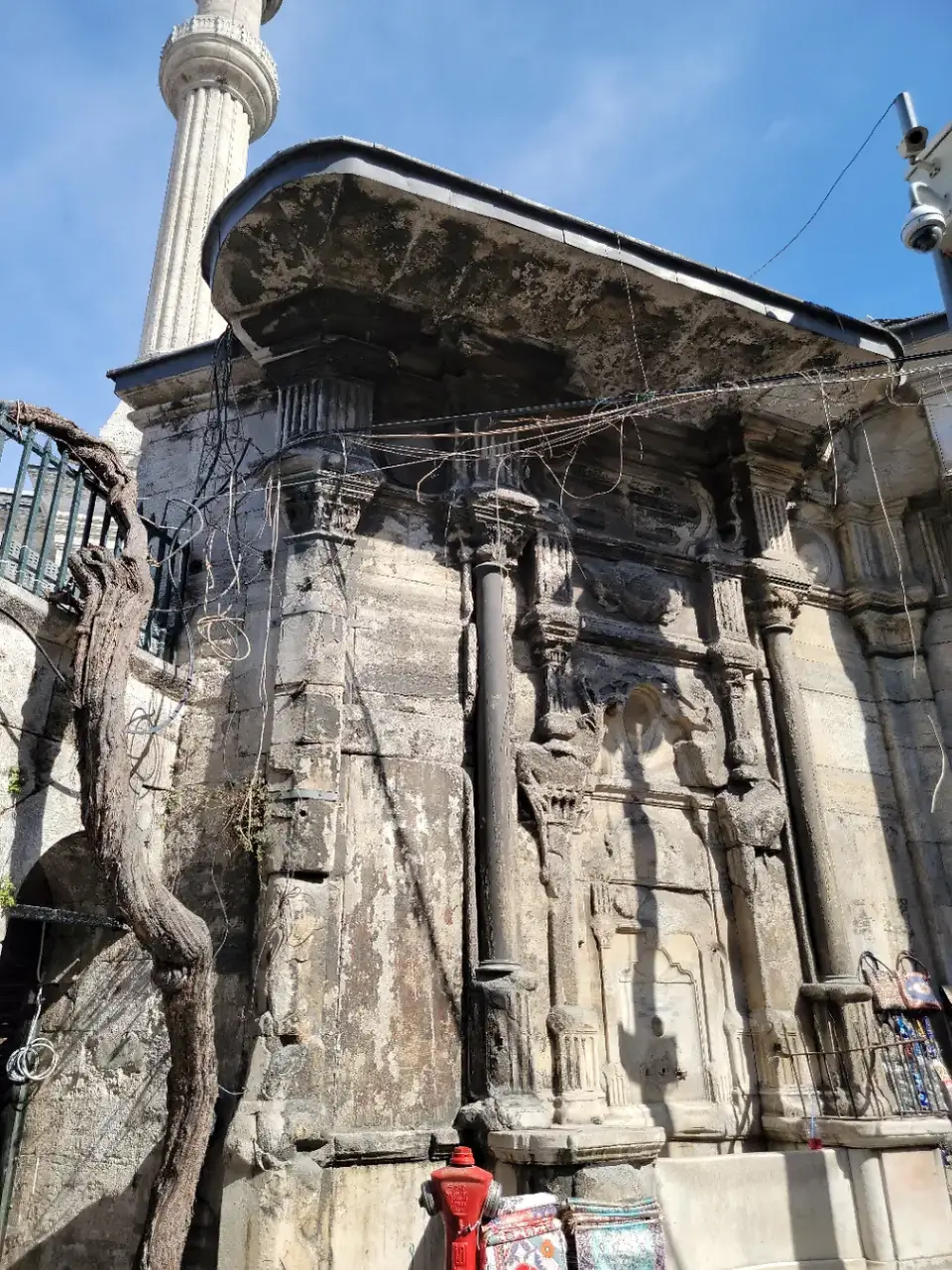 Historic stone masonry wall ruins and minaret rising against a blue sky near the Grand Bazaar in Istanbul, Türkiye.
