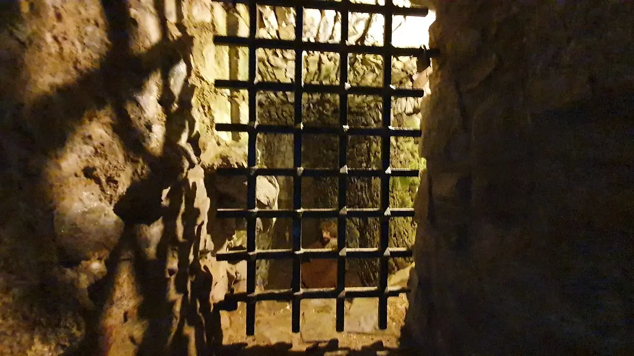 Stone passage at Urquhart Castle ending at a metal grate, with light coming through from outside.