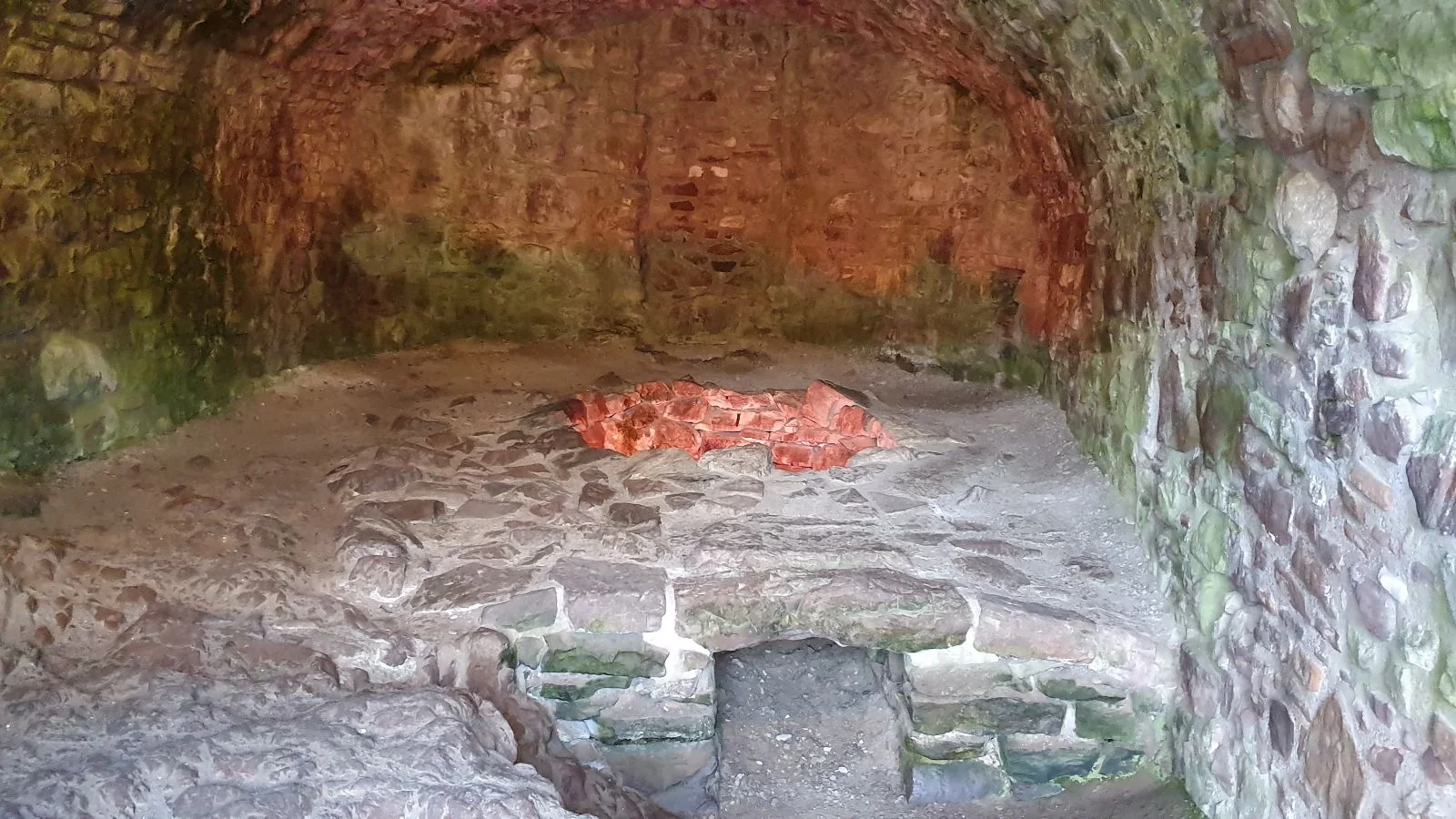 Large stone fireplace inside Urquhart Castle with a fire burning on the hearth.