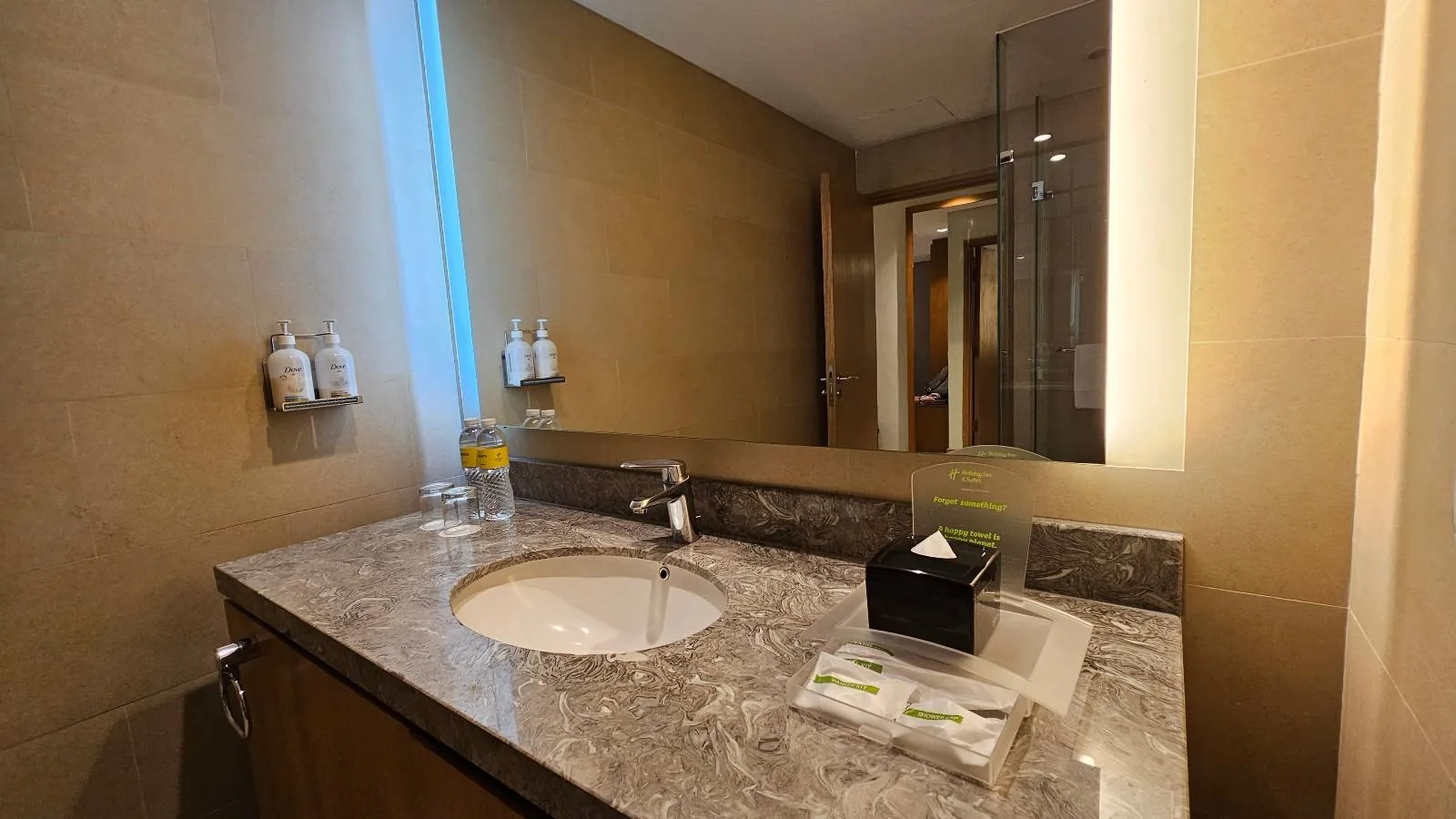 Modern bathroom with a glass-enclosed shower, white toilet, large mirror, wooden vanity with sink, towels on a rack, and toiletries on the wall. The space is well-lit and neatly organized.