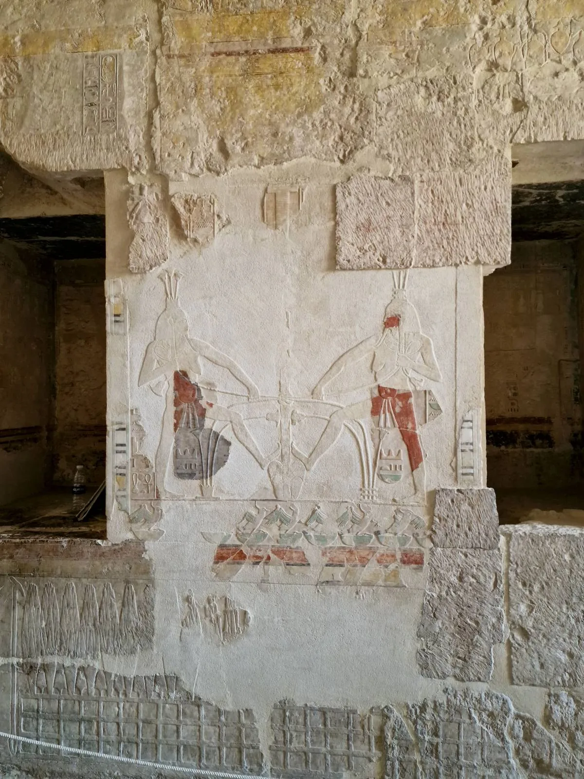 Ancient Egyptian wall painting depicting two figures and hieroglyphics, with visible signs of wear and erosion.