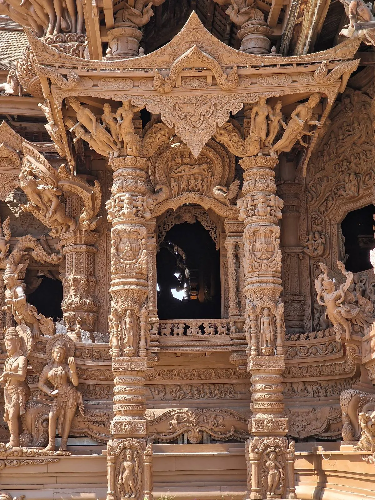 Intricately carved wooden structure featuring detailed sculptures and ornate pillars, showcasing traditional architectural design with elaborate patterns and figures.