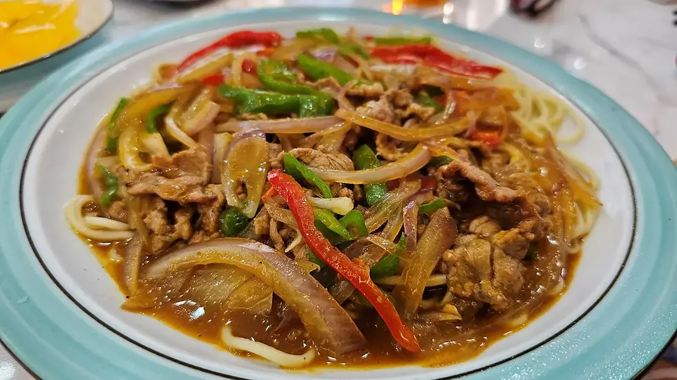 A dish of stir-fried beef with bell peppers, onions, and sauce over noodles on a white and teal plate. Bright colors add a savory appeal.