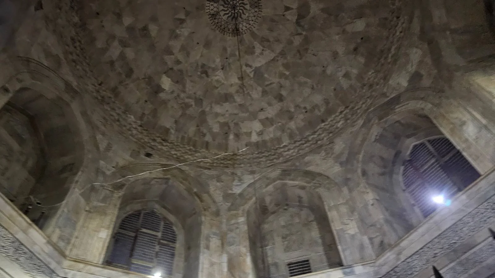 Stone dome ceiling with geometric patterns and arched windows, illuminated by soft lighting from the sides, inside an ancient architectural structure.