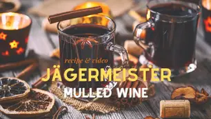 Two glasses of mulled wine with jƤgermeister, garnished with cinnamon sticks and citrus, accompanied by spices and dried orange slices on a wooden table.