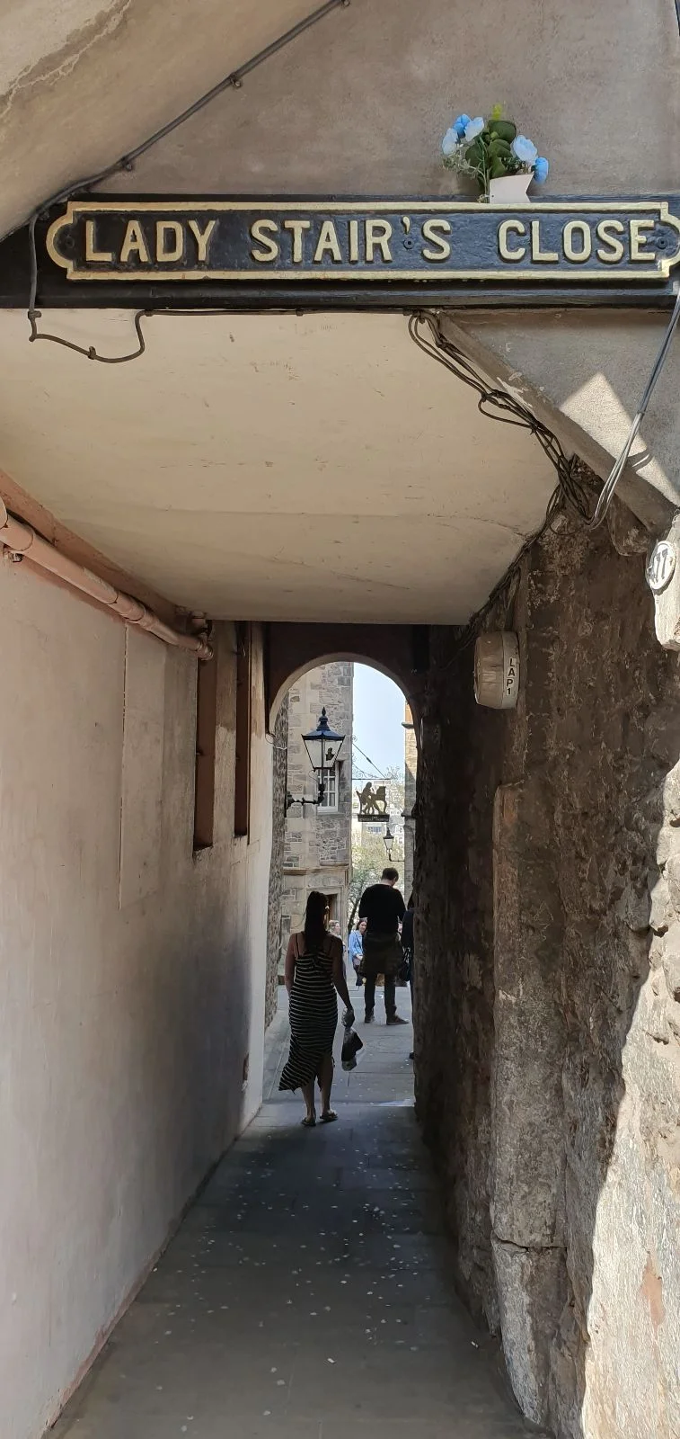 Narrow passageway at Lady Stair’s Close in Edinburgh, with a sign above the entrance and people walking through the archway.