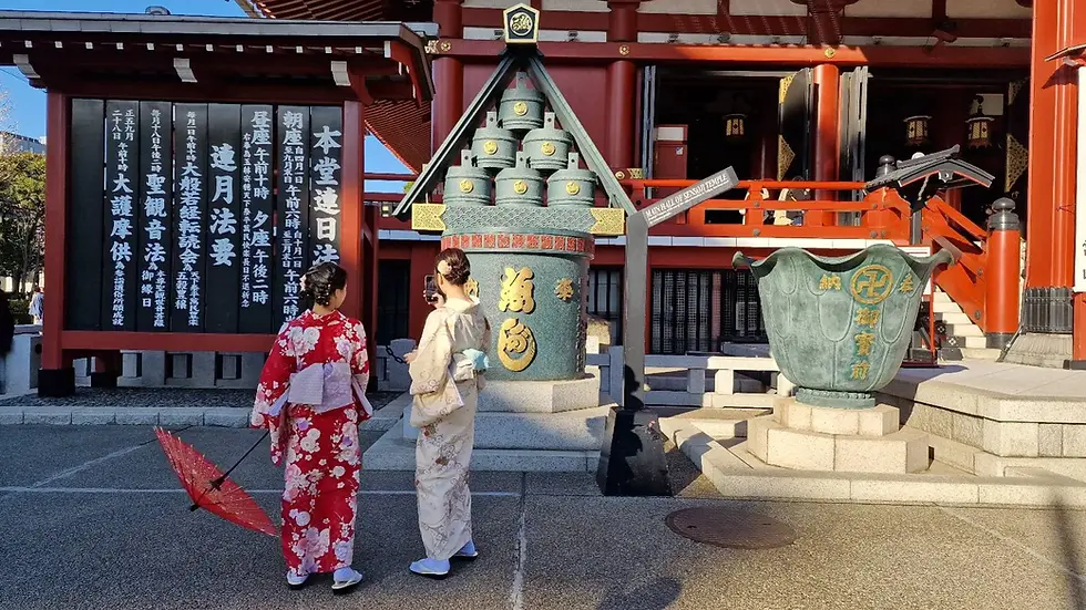 Two people in kimonos stand at a temple, one with a red umbrella. Japanese text is visible. The scene is serene with red building details.