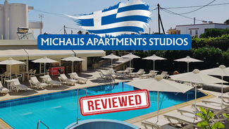 Poolside area with lounge chairs, umbrellas, and a snack bar. Sign reads "Michalis Apartments Studios." Bold "REVIEWED" stamp overlay.