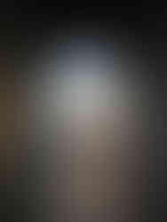 A sunset view through a large arched stone doorway, with several people silhouetted against the light, overlooking a body of water and buildings in the distance.