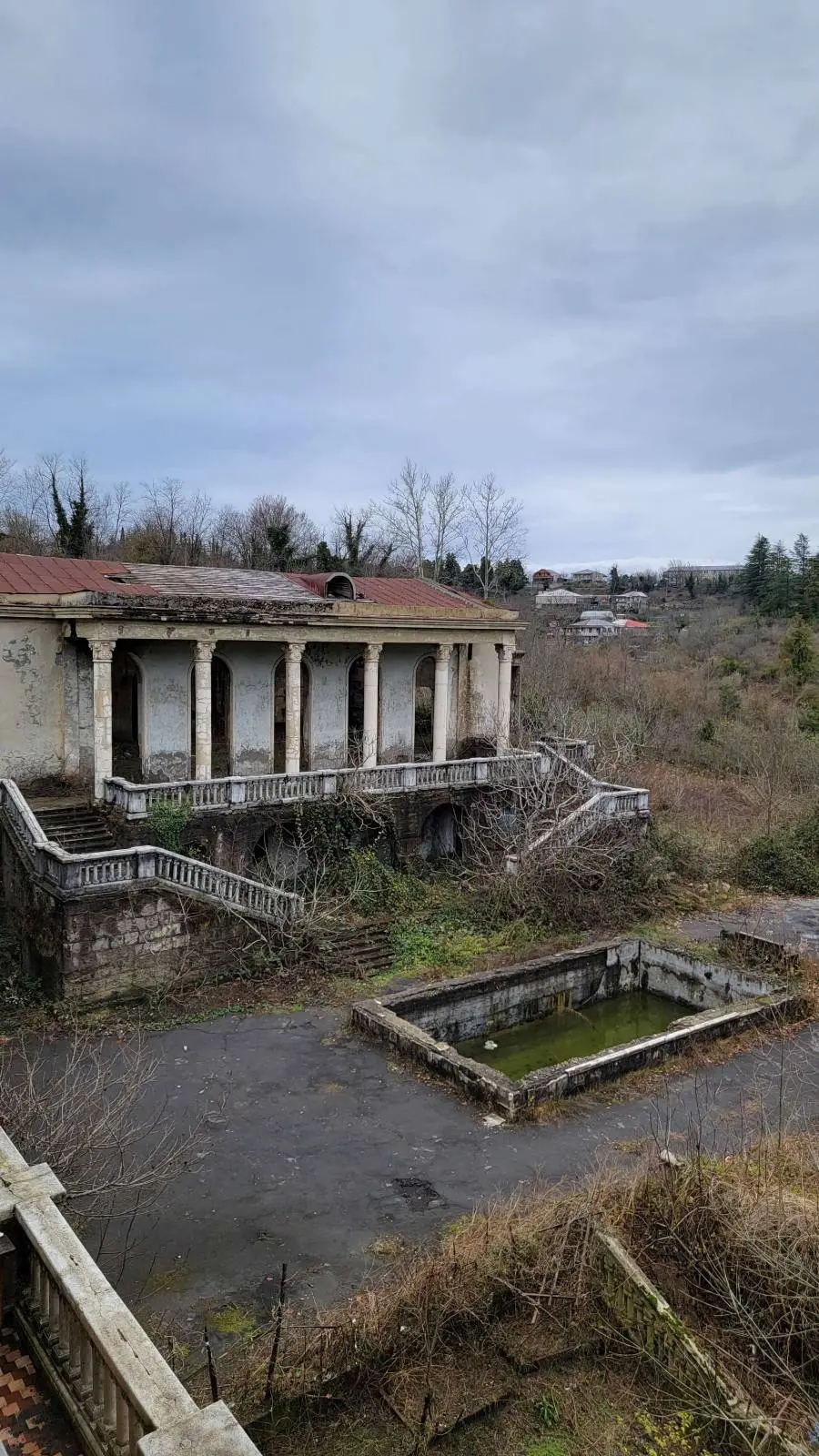 Abandoned building with overgrown vegetation under a cloudy sky.