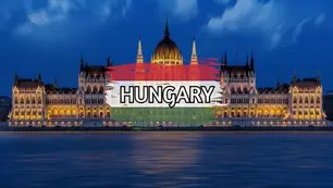 Illuminated hungarian parliament building at night with a blurred sky and hungary's flag superimposed below.