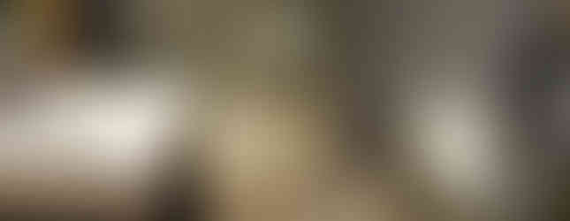 Modern bathroom with a glass shower enclosure, white sink on a dark vanity, wall-mounted toilet, and a beige tiled floor. A towel hangs on the glass shower door.