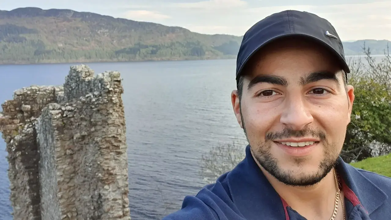 Leon taking a selfie at Urquhart Castle with Loch Ness and surrounding hills in the background.