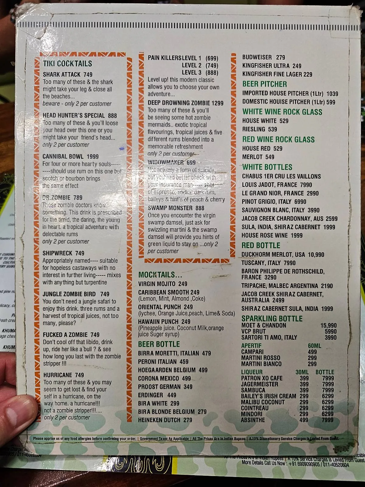 A hand holds a restaurant menu featuring sections for hot beverages, cold beverages, breakfast plates, bakery items, hot cereals, juices, and sides, with various options and prices listed in black and green text.