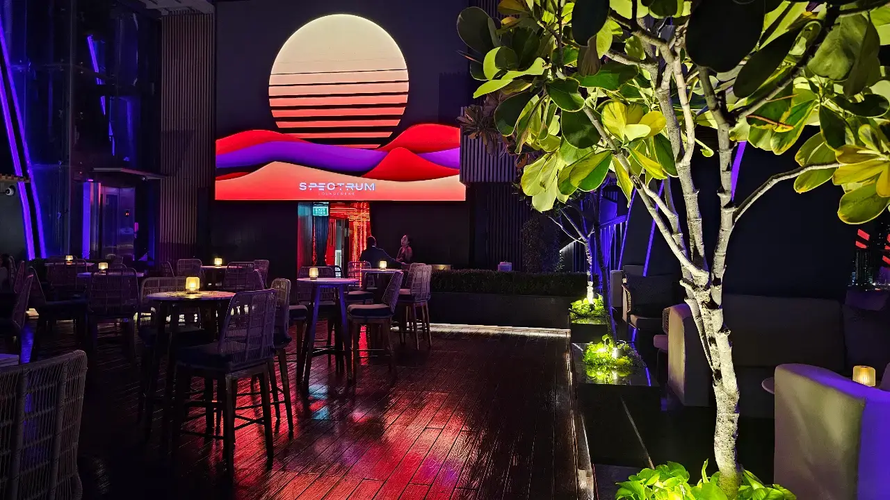 Outdoor rooftop seating beneath a glowing circular light feature and tropical greenery.