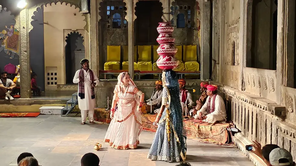 A woman performs balancing pots on her head in a traditional dance. Musicians sit nearby. The setting is an ornate, historical venue.