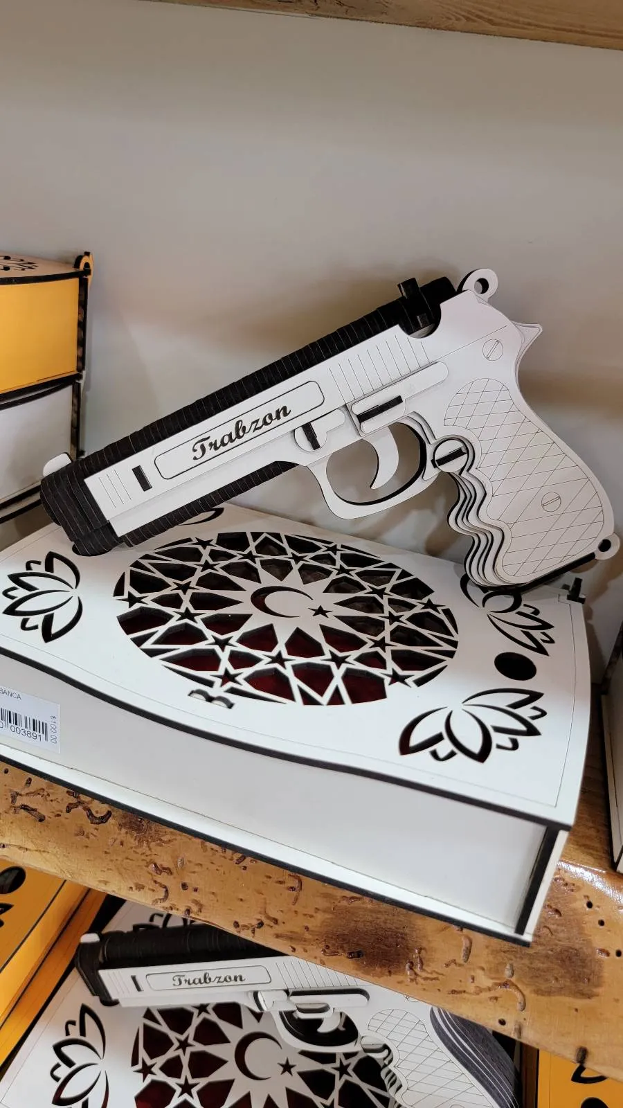 A white and black toy gun lies on a decorative white and black box on a wooden surface.