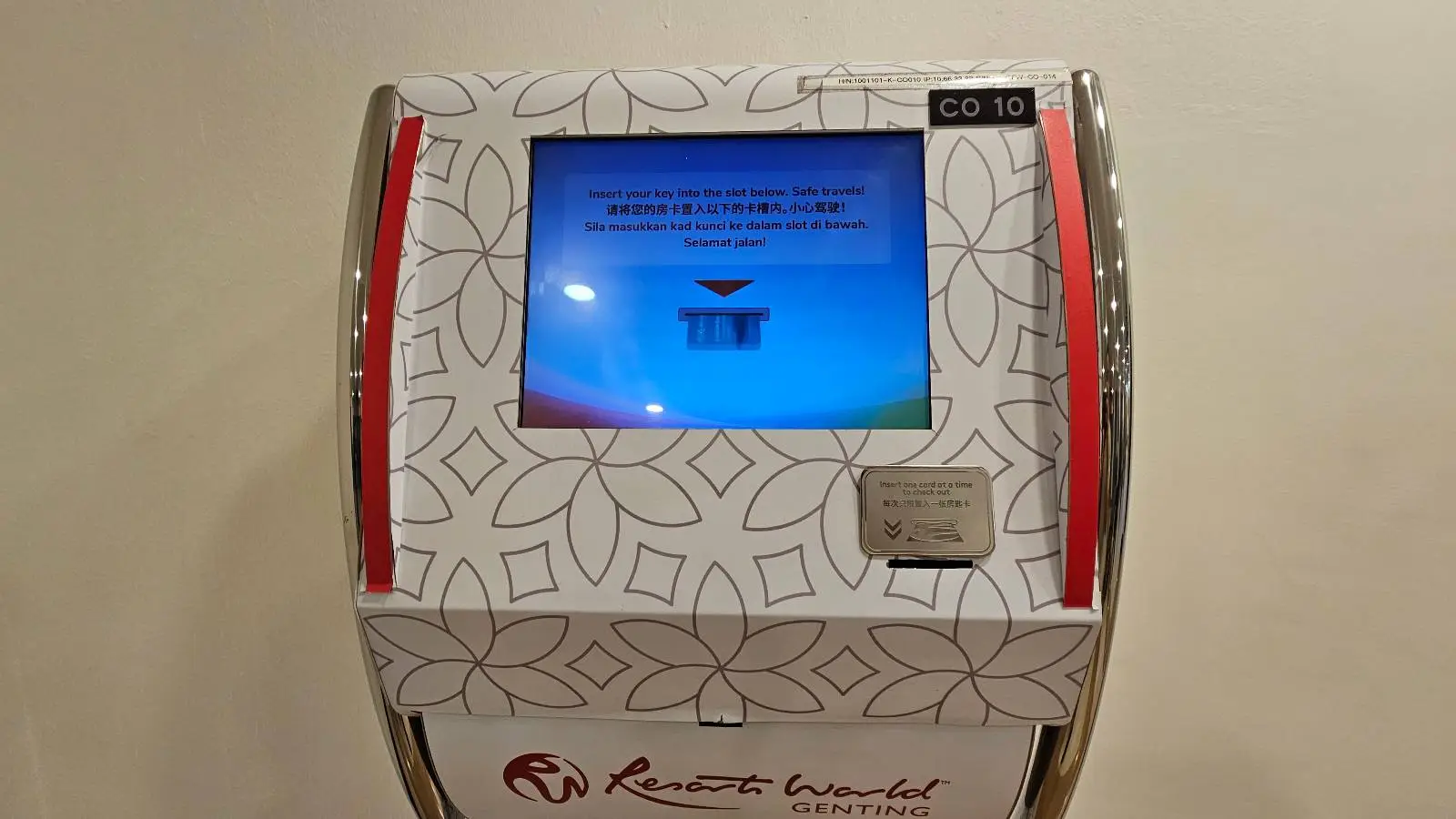 Self-checkout kiosk at Resorts World Genting with floral pattern and screen instructing key insertion. Red accents and multilingual text.