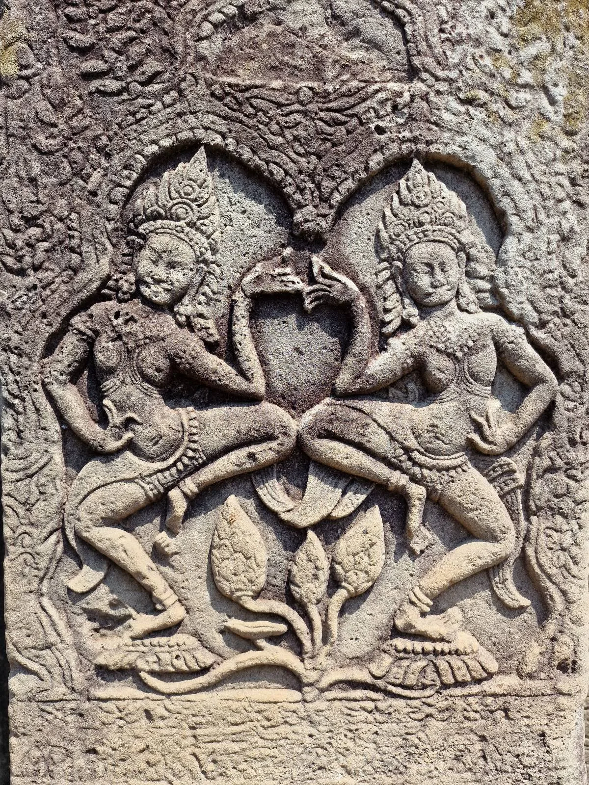 Detailed stone carving depicting two dancing female figures in traditional attire, facing each other with one leg raised, surrounded by ornate floral and arch patterns.