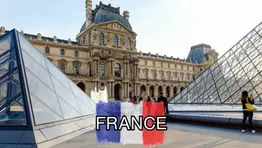 Glass pyramids in front of the Louvre Museum in Paris with the word "FRANCE" over a painted French flag.