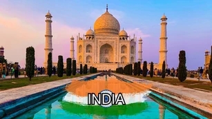 The Taj Mahal at sunset with its reflection in a long pool, surrounded by gardens and visitors. The word "INDIA" and an Indian flag overlay are at the bottom of the image.