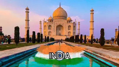 The Taj Mahal at sunset with its reflection in a long pool, surrounded by gardens and visitors. The word "INDIA" and an Indian flag overlay are at the bottom of the image.