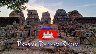 Ancient stone temple under a blue sky, with a Cambodian flag overlay. Text reads Prasat Phnom Krom, exuding a historical ambiance.