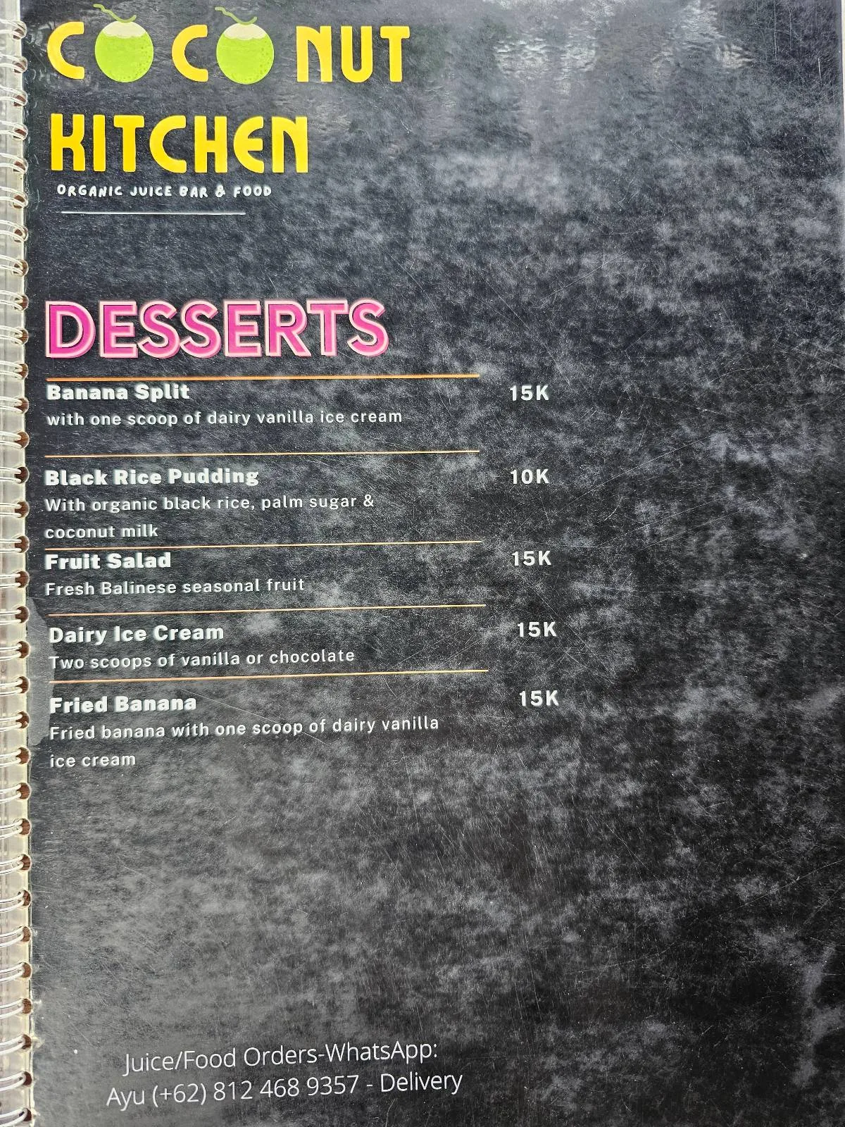 Menu from Coconut Kitchen featuring desserts like banana split, black rice pudding, sticky rice, fruit salad, and fried banana. The background is a dark textured surface with yellow and white text.