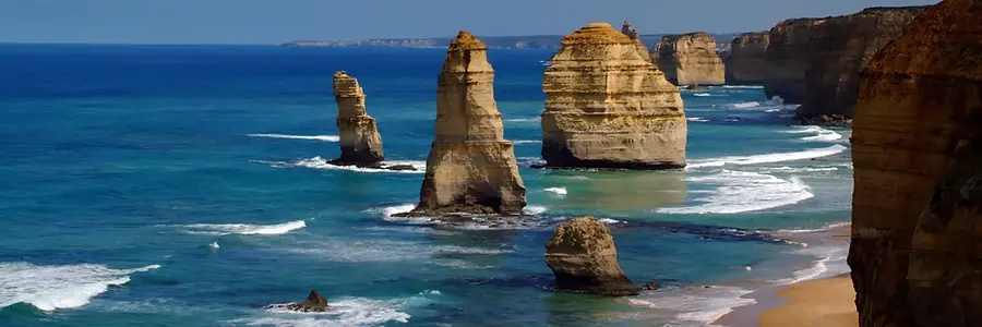 The Twelve Apostles rock formations standing in the bright blue ocean along the rugged coastline of Victoria, Australia on a sunny day.