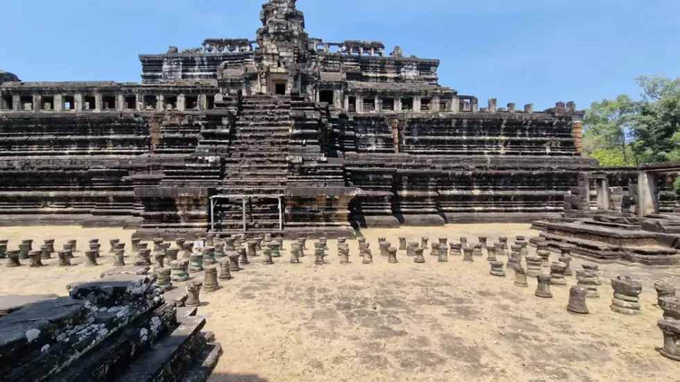 Ancient stone temple with steep steps and columns in foreground under a clear blue sky. Surrounding greenery adds contrast to the scene.