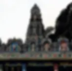 Colorful Hindu temple facade with intricate deities and patterns. Set against a backdrop of lush greenery and a clear sky. Serene mood.