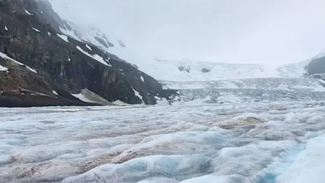 Close-up view of the Athabasca Glacier in Alberta, Canada, with textured ice formations and surrounding mountain rock faces.