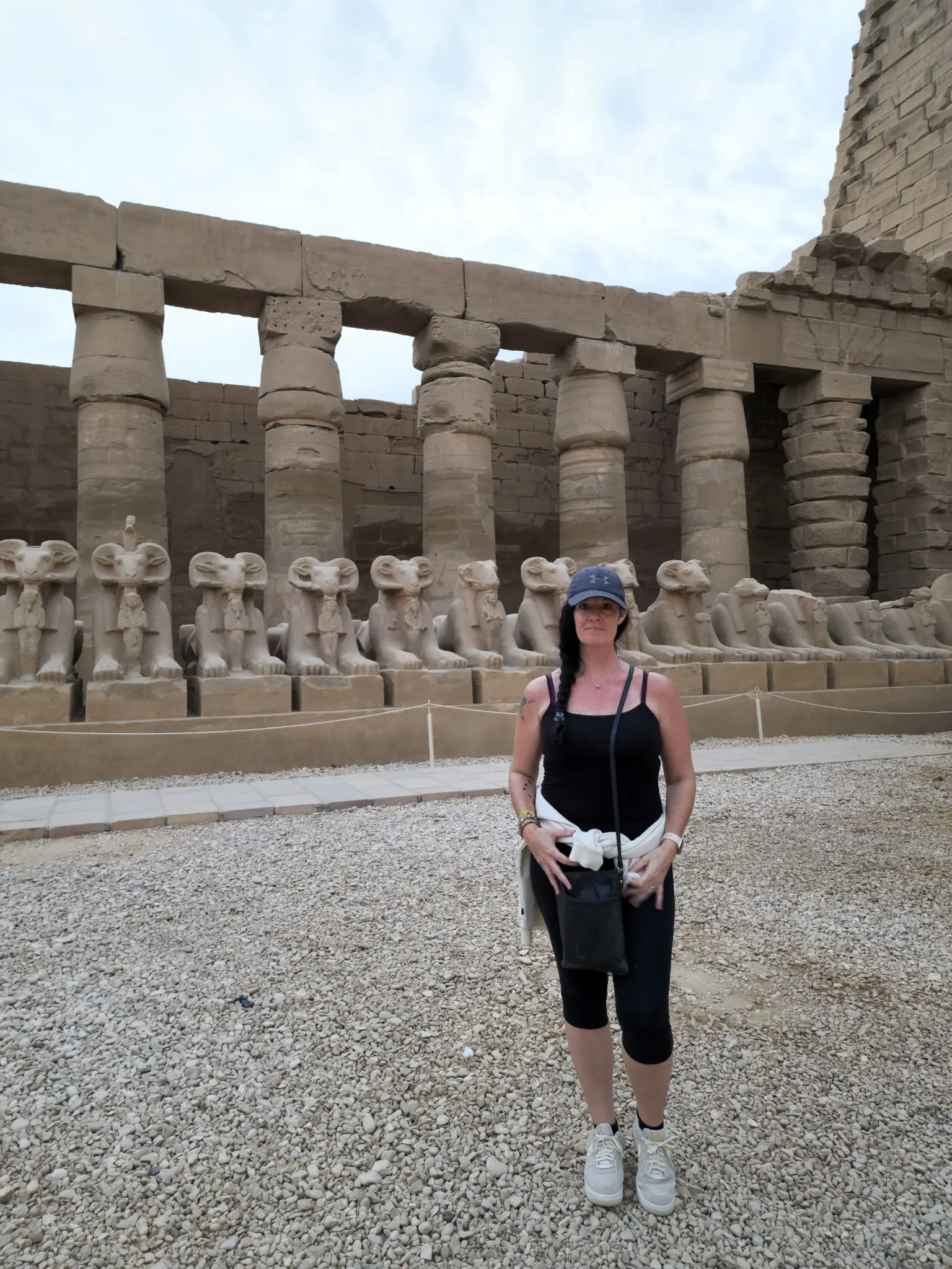A person stands in front of a row of ancient statues and columns at a historic site.