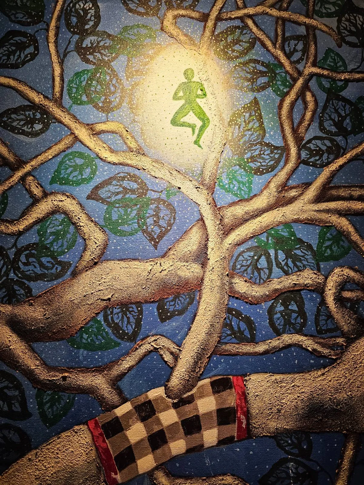 A glowing green figure is curled up inside a bright orb atop tree branches, surrounded by green leaves against a blue background. One branch is wrapped in a checkered black, white, and red cloth.