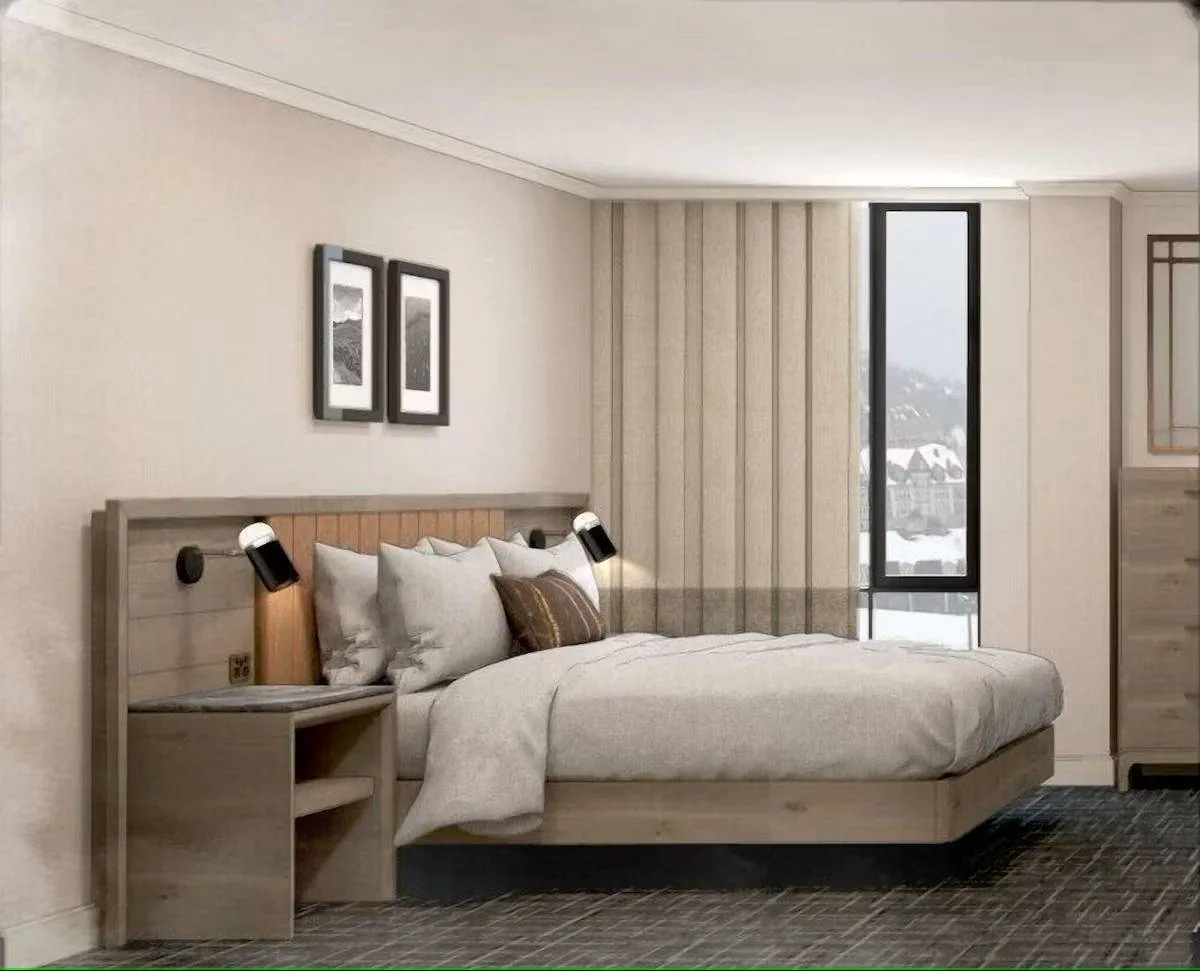 Modern bedroom with a large bed featuring white bedding and pillows. There are two wall-mounted black lamps on either side of the headboard. The room has light-colored walls, two framed pictures above the bed, and a window with a snowy view.