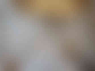 A minimalistic bedroom features a double bed with white bedding, flanked by pendant lights. Above the bed, a decorative macrame hangs on the wall. To the left, a hammock chair is suspended. Soft lighting creates a cozy atmosphere.