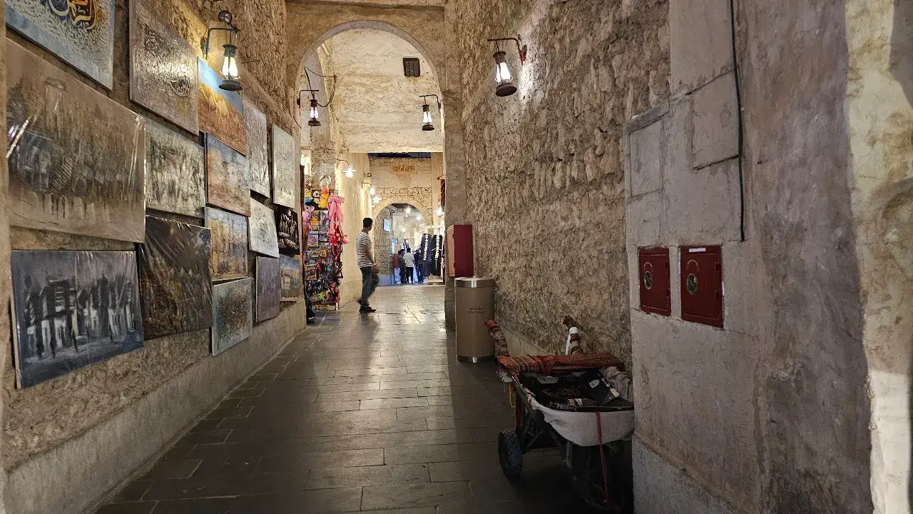 Narrow stone alleyway lined with traditional market stalls and lanterns at Souq Waqif in Doha, Qatar.