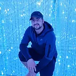 Smiling portrait of Leon, co-founder of Closer Lives, wearing a dark hoodie and a cap against a vibrant blue textured background, set in a circular frame.