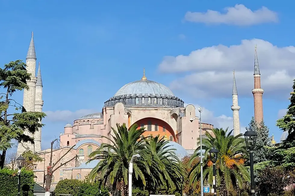 The image shows the Hagia Sophia with its large dome and minarets, surrounded by trees, under a clear blue sky.